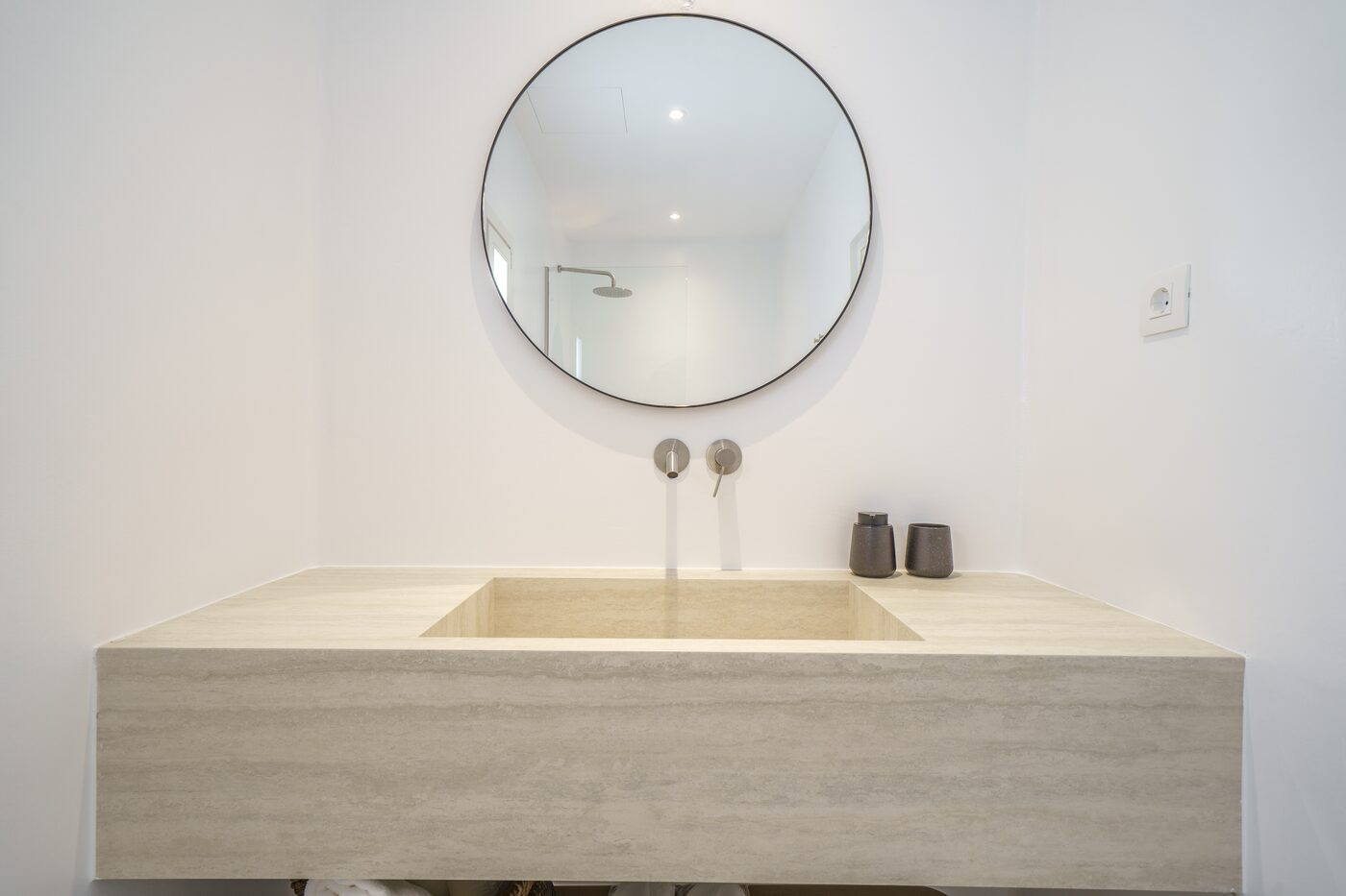 Travertine washbasin and round mirror in a Primadonna ensuite bathroom