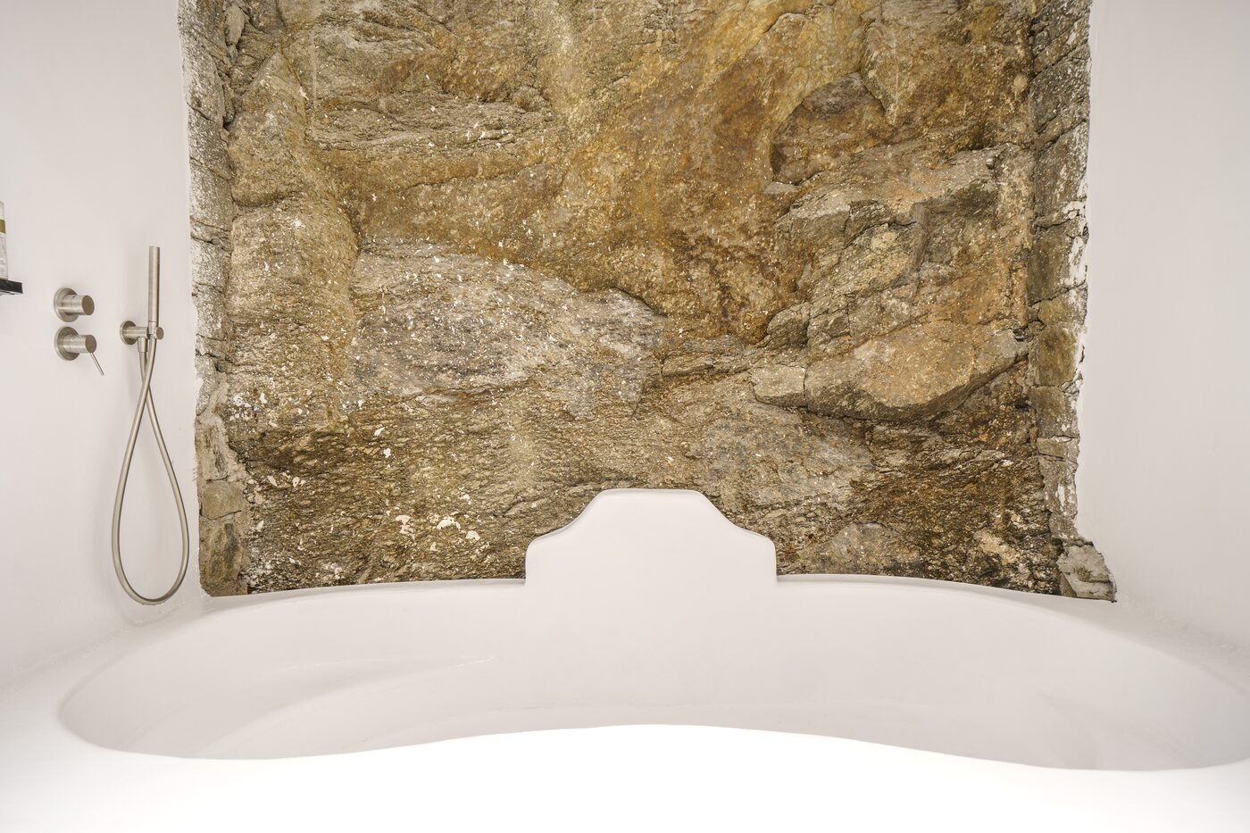 Spa bathroom with a carved stone tub against an exposed rock wall, Mykonos