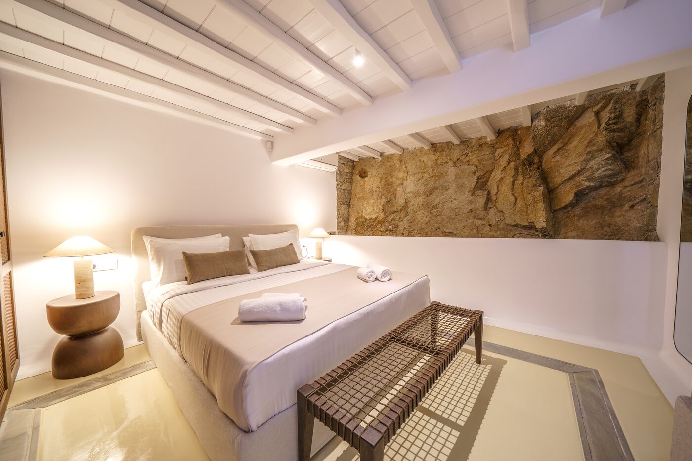 Bedroom set against a natural rock wall with timber joinery at Primadonna, Mykonos