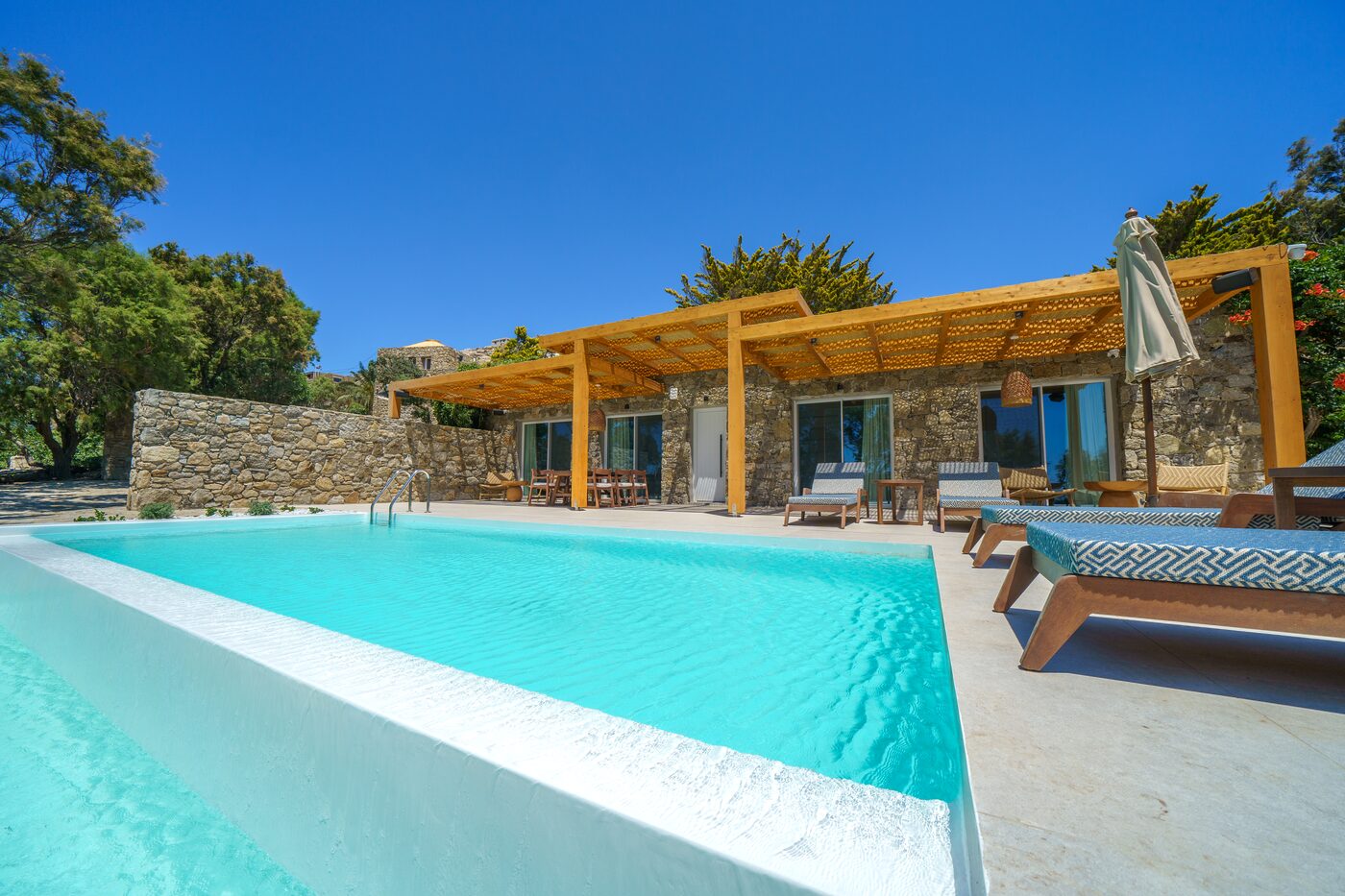 Villa Catherine horizon pool and stone-clad villa facade with sun loungers, Mykonos